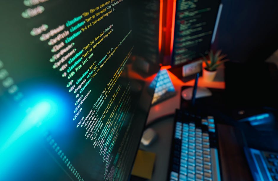 A silver MacBook Pro laptop placed on a dark wooden desk displaying a screen filled with lines of programming code highlighted in yellow and green, indicating a software development or web coding proc